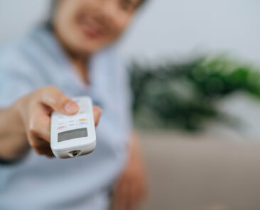 Close up and Selective focus hand of woman holding and use remote control to open aircondition in living room at home