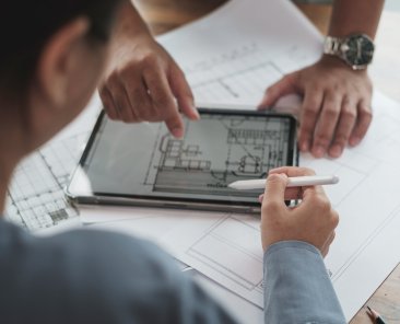 Selective focus hand holding pencil. Architect or Engineer team designer discussing detail drawing on digital tablet.